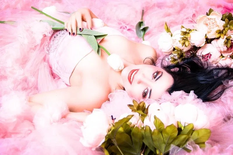A woman reclining in a dreamy, romantic atmosphere of flowers and pink tulle, embodying the radiant, divine feminine energy of a woman who has found her inner peace.