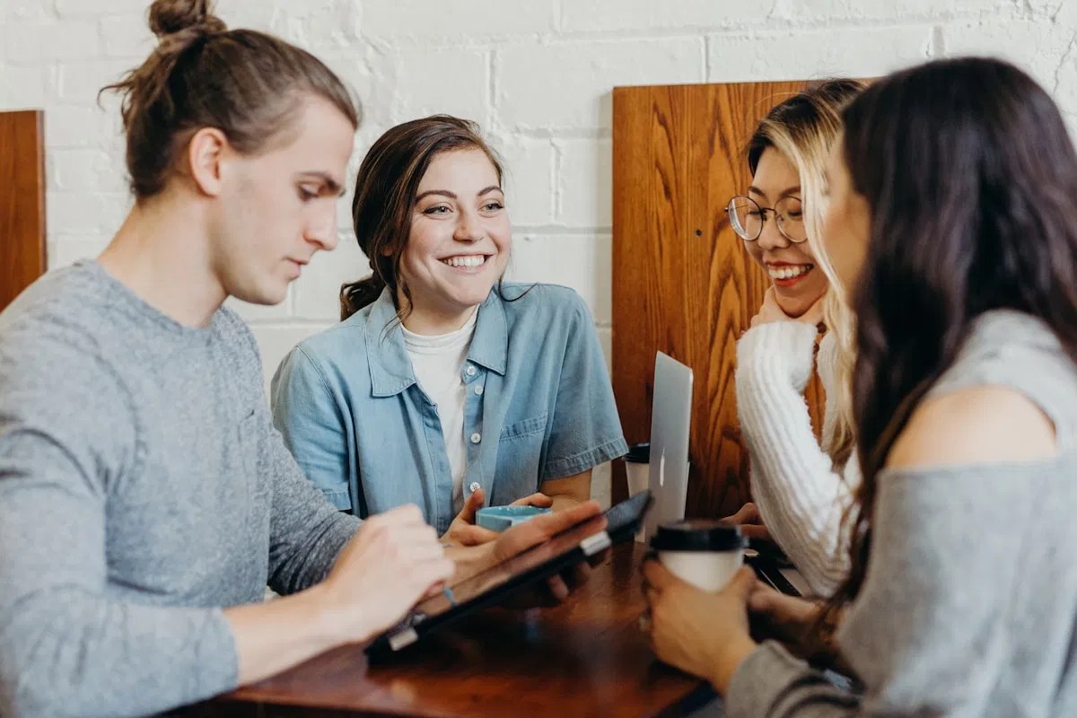 A diverse group of insurance professionals collaborating in a modern office. They are looking at a tablet together, with hand-drawn lightbulbs and checkmarks doodled above their heads to symbolize teamwork and strategy.
