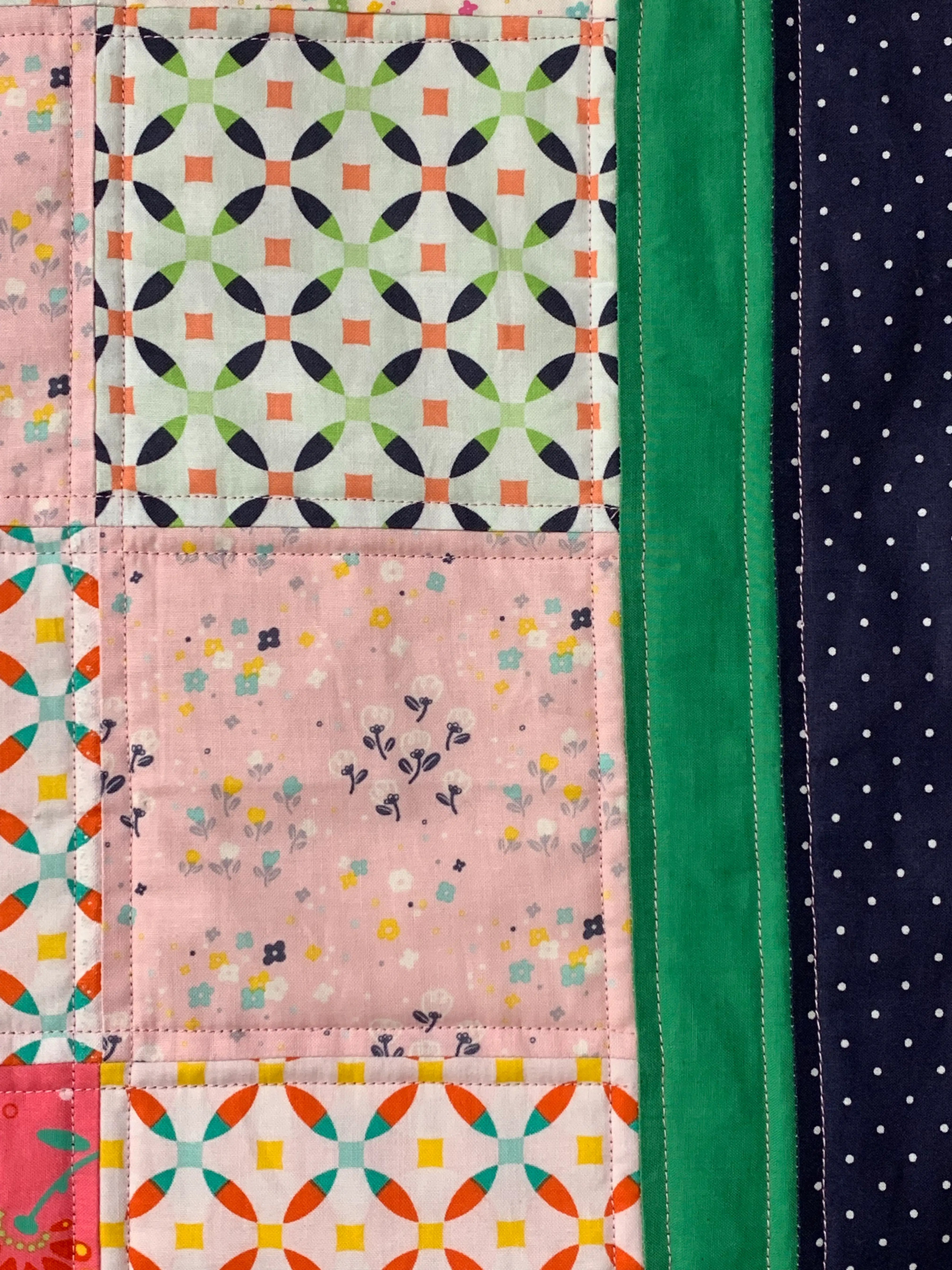 A close-up view of a machine-quilted sampler featuring square patchwork blocks in pastel prints.
