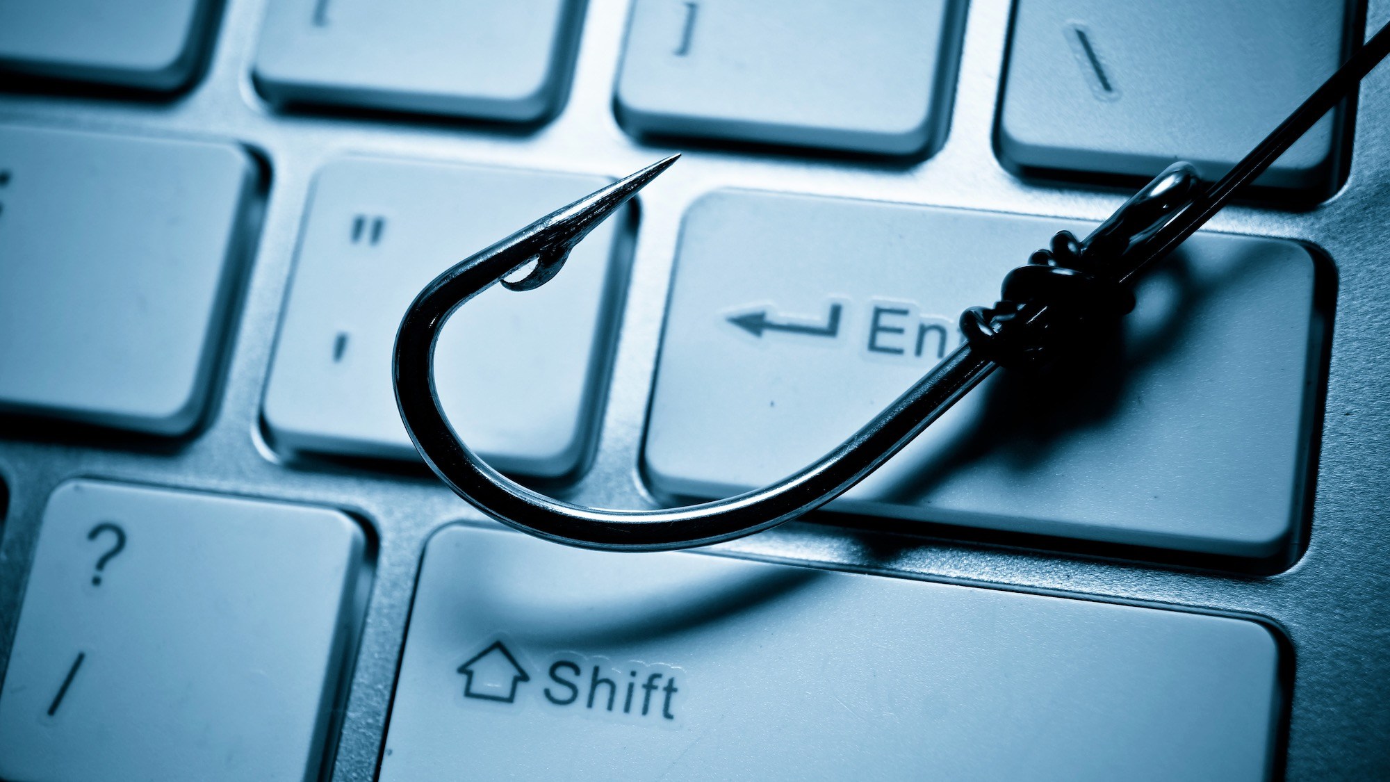 パソコンのキーボードの上に釣り針が置かれており、コンピュータシステムへのフィッシング攻撃を表しています