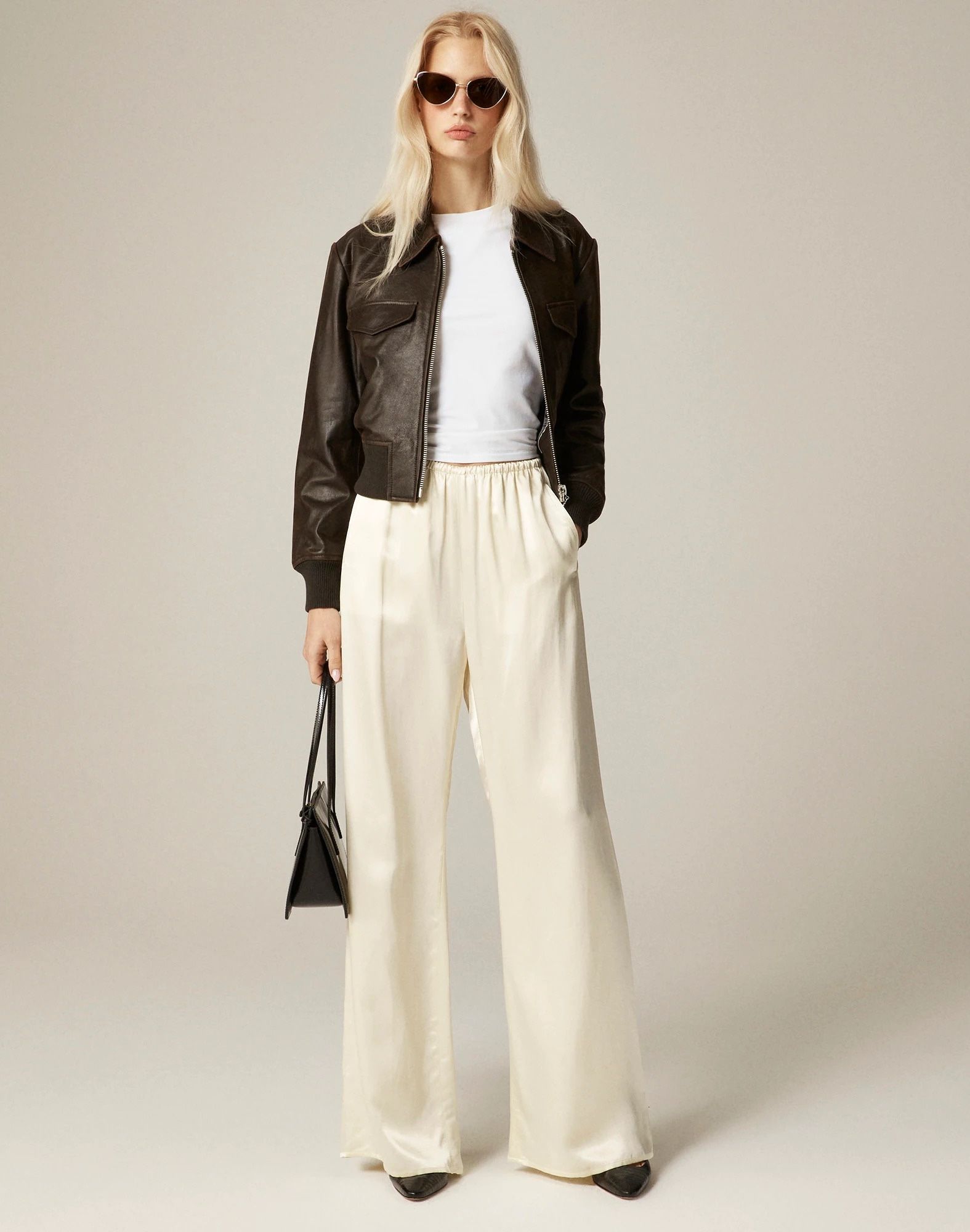J.Crew fall 2025 collection outfit idea with a brown leather jacket, metal-rim sunglasses, a white t-shirt, a cream charmeuse satin drawstring pants, and black shoes