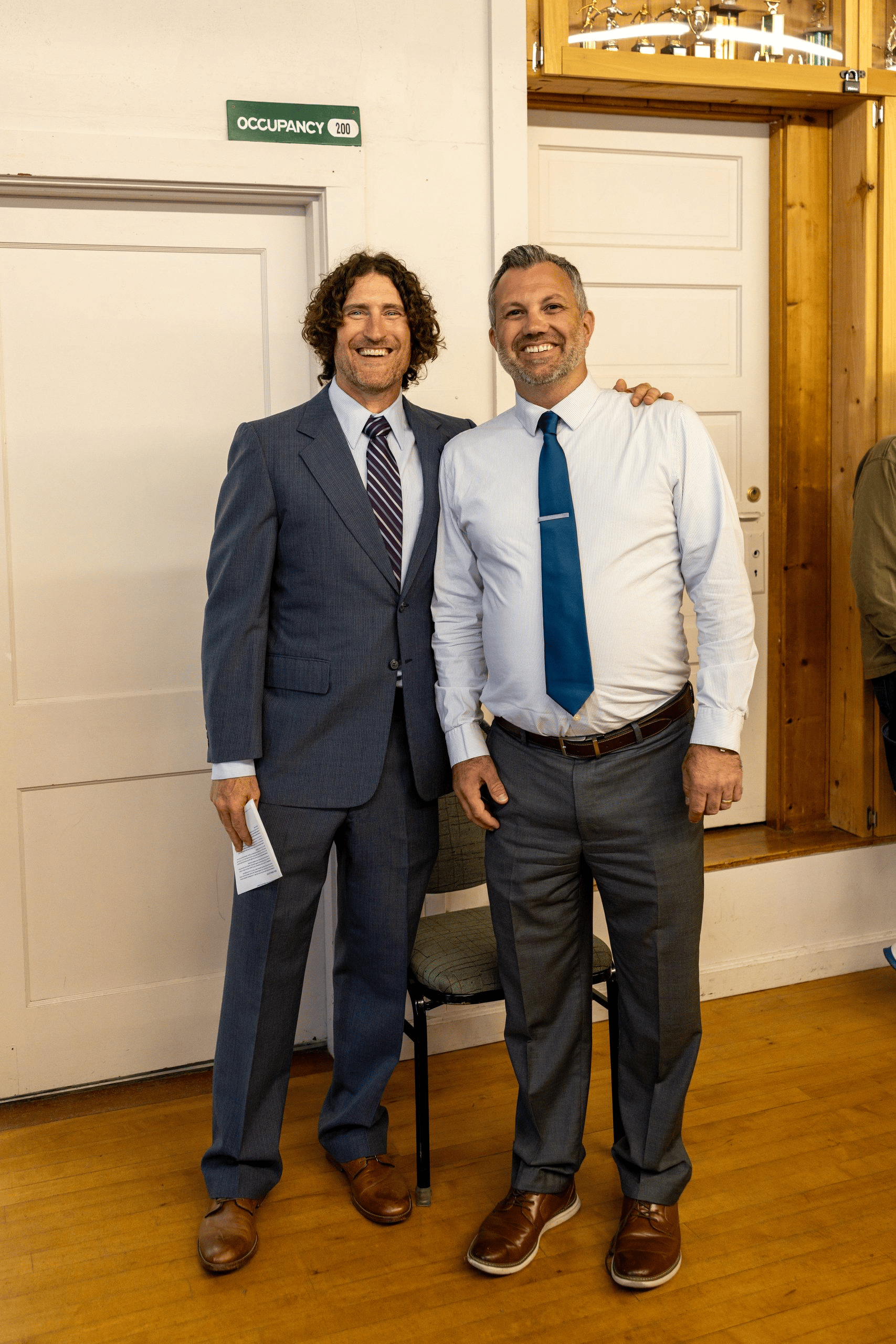 Clallam County commissioner candidates Jake Seegers and Mike French stand together and smile inside the Sequim Prairie Grange. Clallam County District 3 commissioner candidates Jake Seegers and Mike French seated at a table facing a full room at the Sequim Prairie Grange.