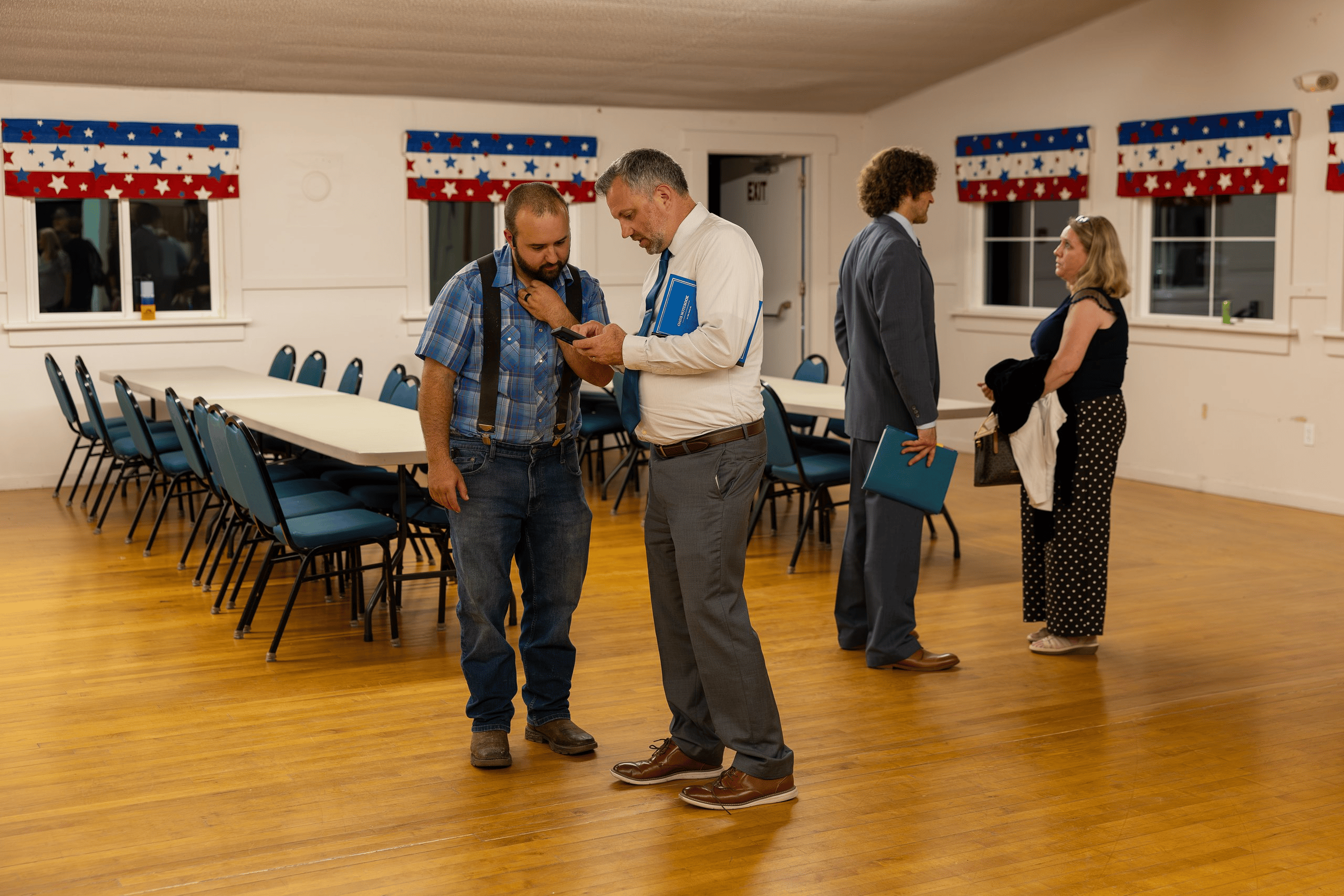 Mike French reviews a phone with an attendee while Jake Seegers speaks with another attendee inside the grange hall. Clallam County District 3 commissioner candidates Jake Seegers and Mike French seated at a table facing a full room at the Sequim Prairie Grange.