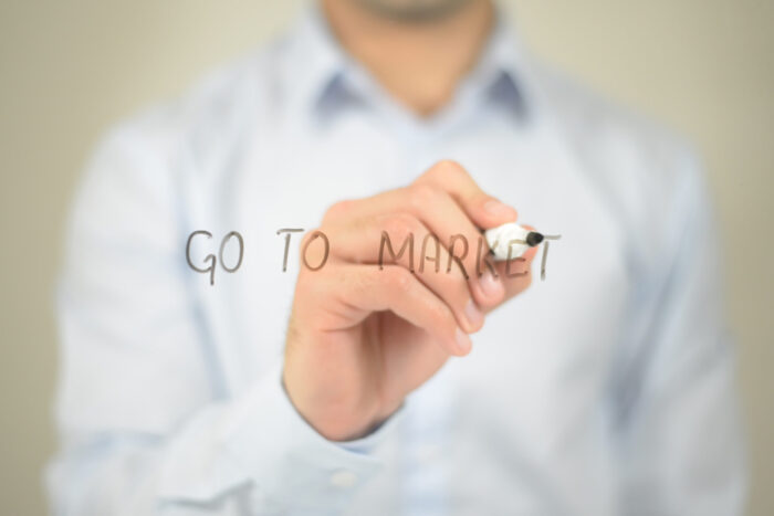 Person writing "Go to Market" on glass.