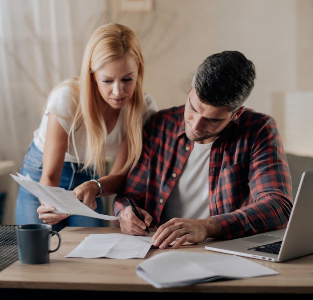 Man and woman at a desk checking their bills next to a laptop