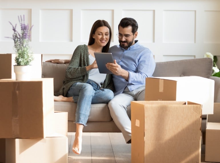 Couple seated on couch using a tablet next to packed boxes
