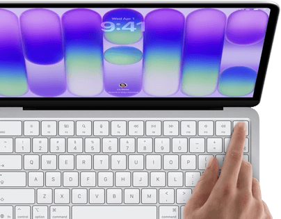 MacBook Neo, silver color, showing login screen, person's finger on Touch ID sensor in top-right corner of keyboard