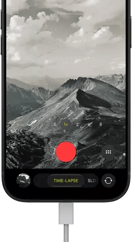 iPhone 18 Pro, front exterior, displaying a mountainous landscape, with the camera mode overlay in Time-Lapse mode, with power cable attached to charging port