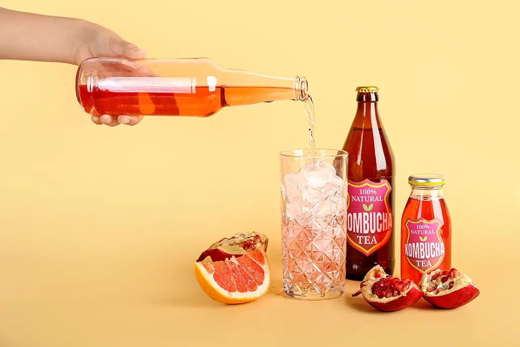 Kombucha sendo servida em um copo de vidro com bastante gelo.