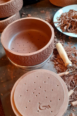 A clay pottery in the process of making with pottery tools and clay shavings around on the table.