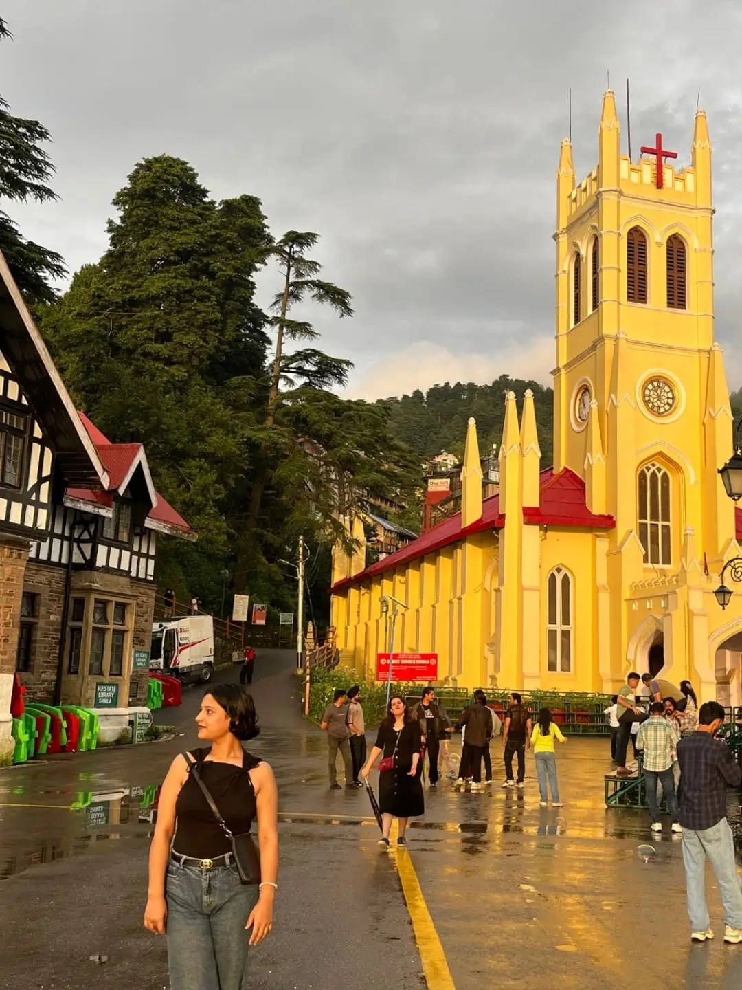 An exterior shot of the Jakhu Temple in Shimla, with a large, vibrant orange statue of Lord Hanuman standing tall against a clear blue sky.