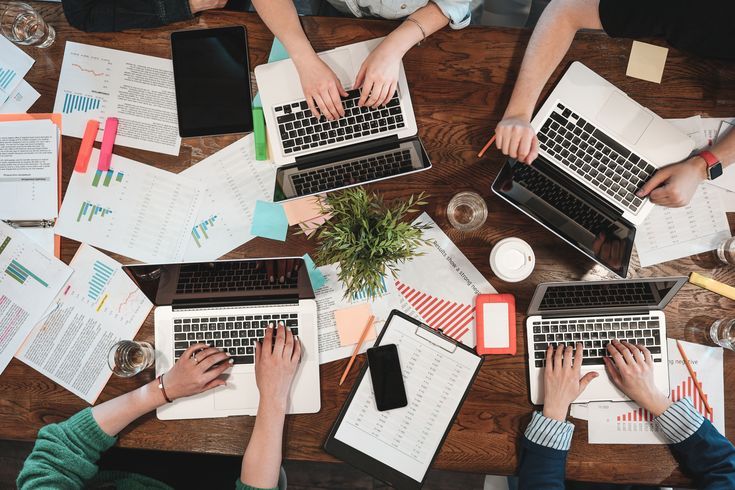 Top view of young coworking people are working on laptops and paper documents. Group of college students using laptop while sitting around table. Team of hipsters making new great startup