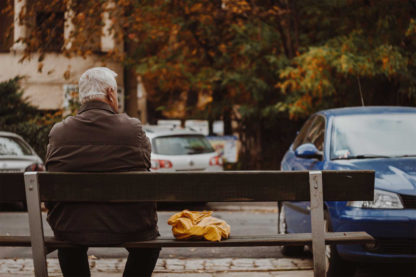 Older man sitting on a bench near a parking lot - ChangingAging.org