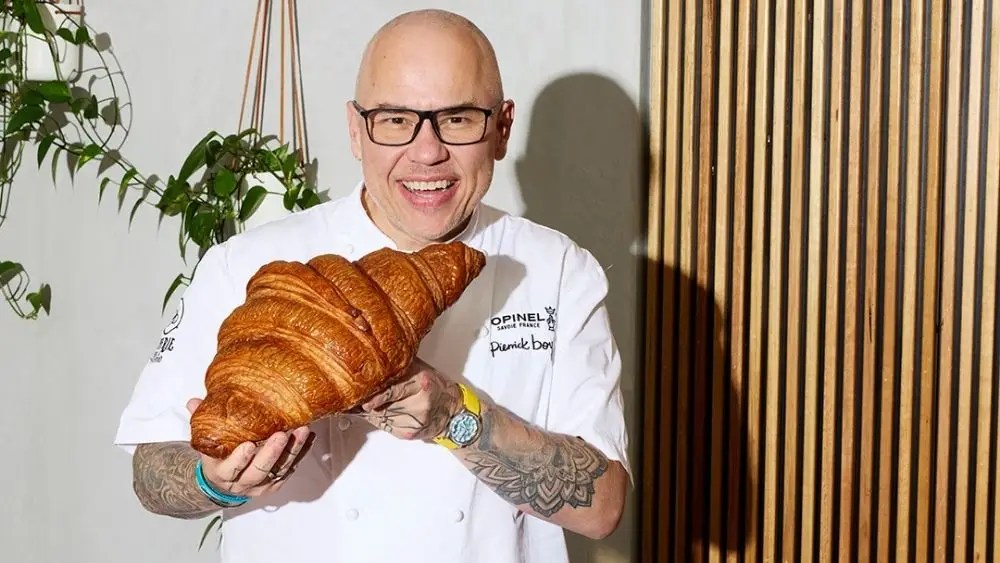 Reverie Cafe chef smiling while holding an oversized freshly baked croissant.