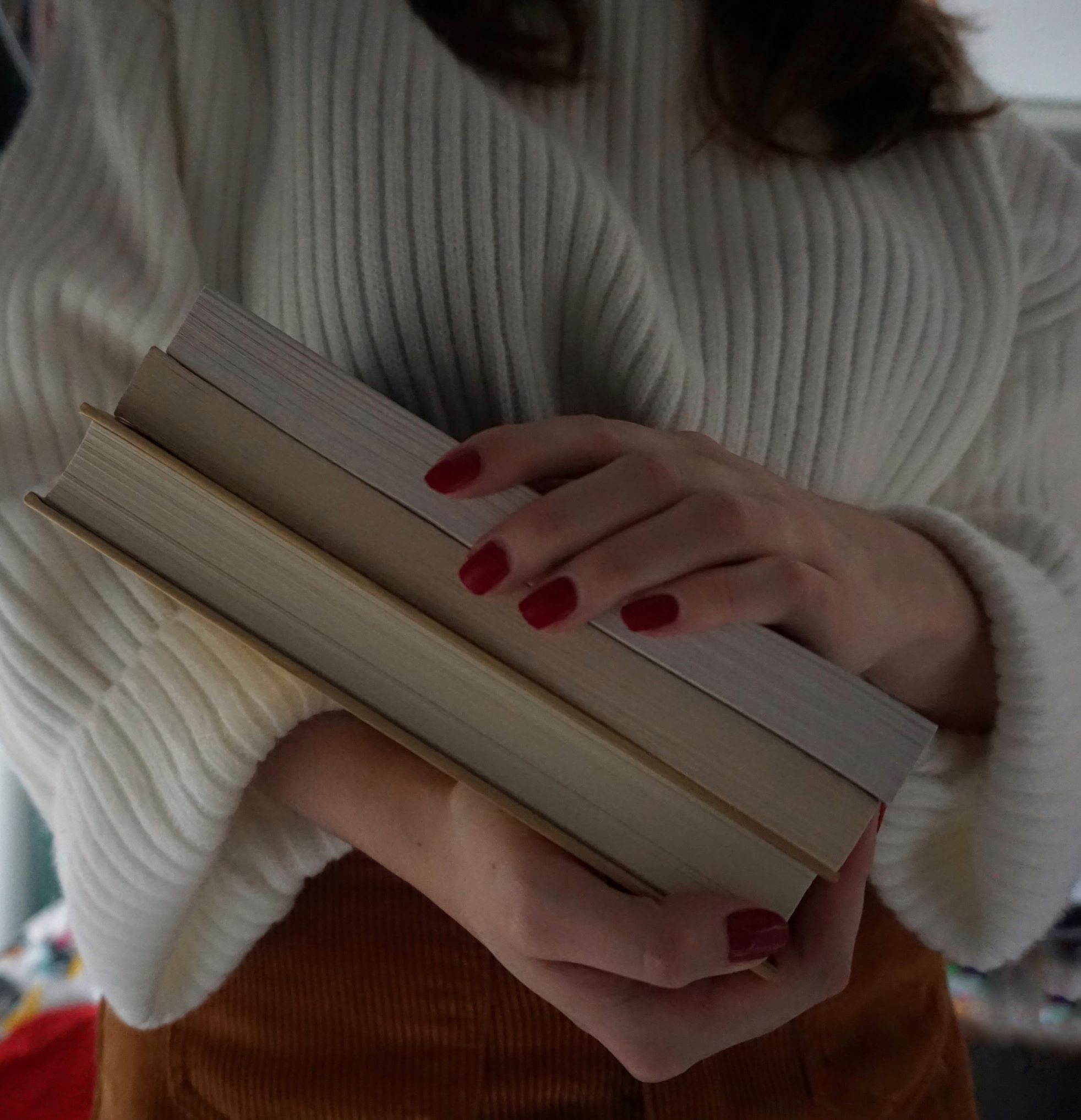 girl holding three books, red nails