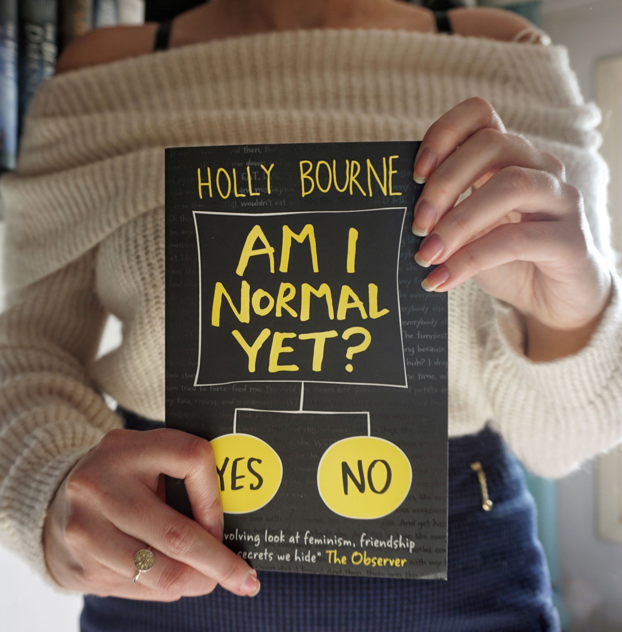 A girl holds the book 'Am I Normal Yet?', dressed in blue skirt and white pullover.