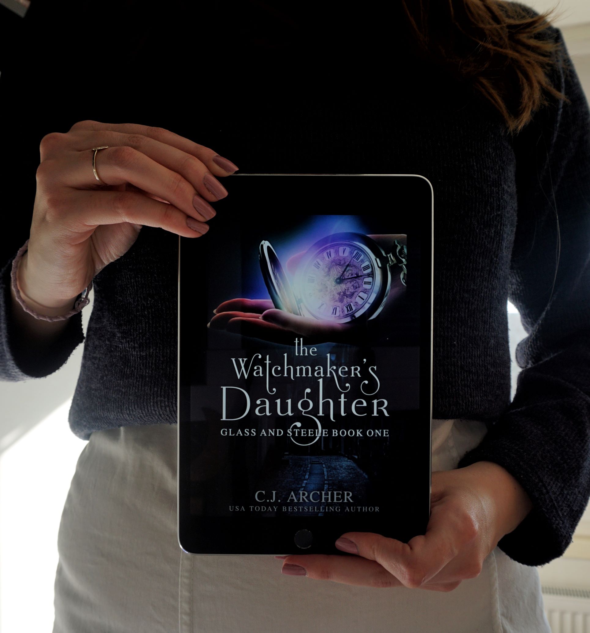 Female book blogger, dressed in white skirt and dark blue pullover presents the e-book A Watchmaker's Daughter