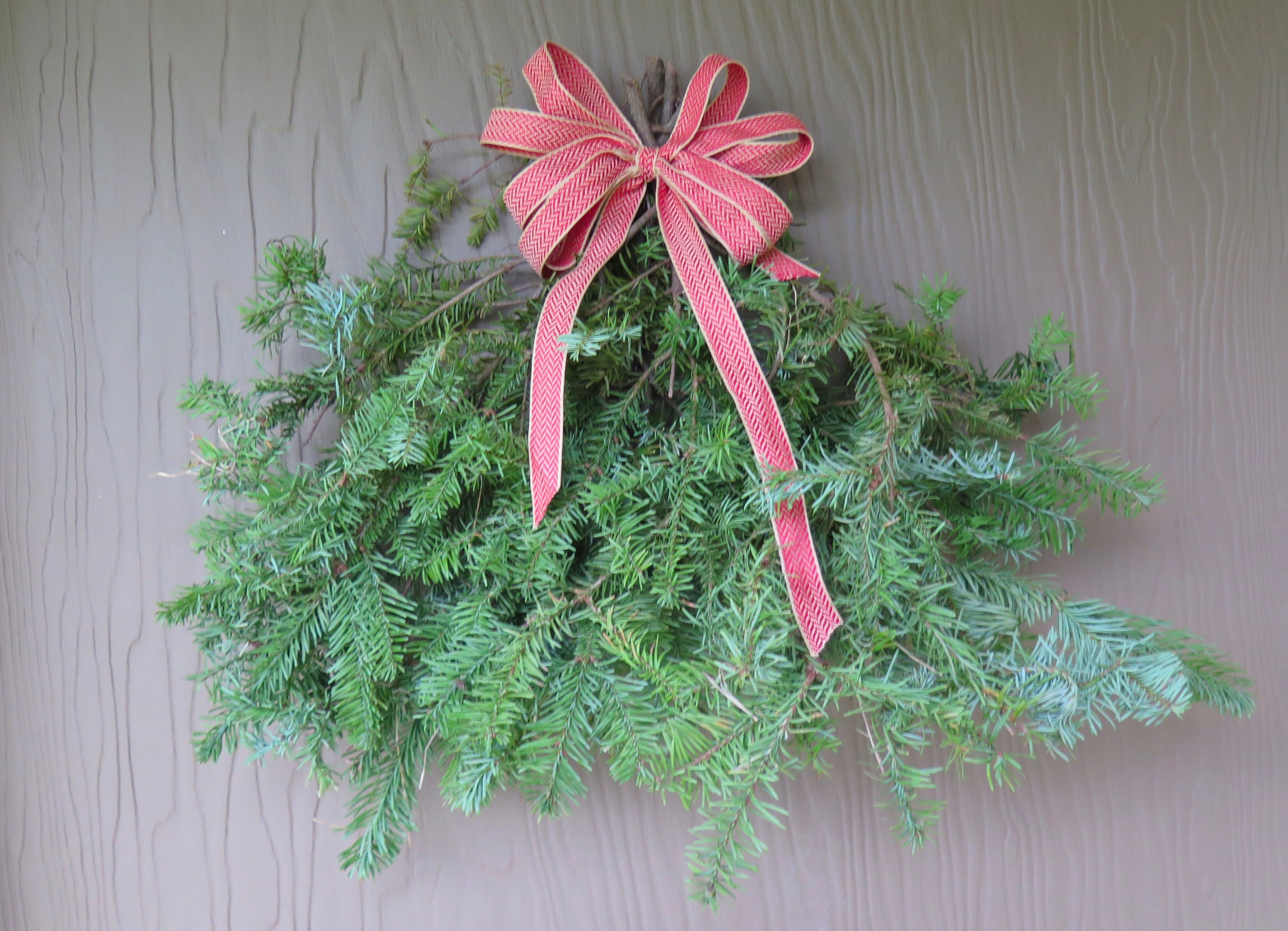 Finished evergreen spray with a ribbon bow hanging on our front door.