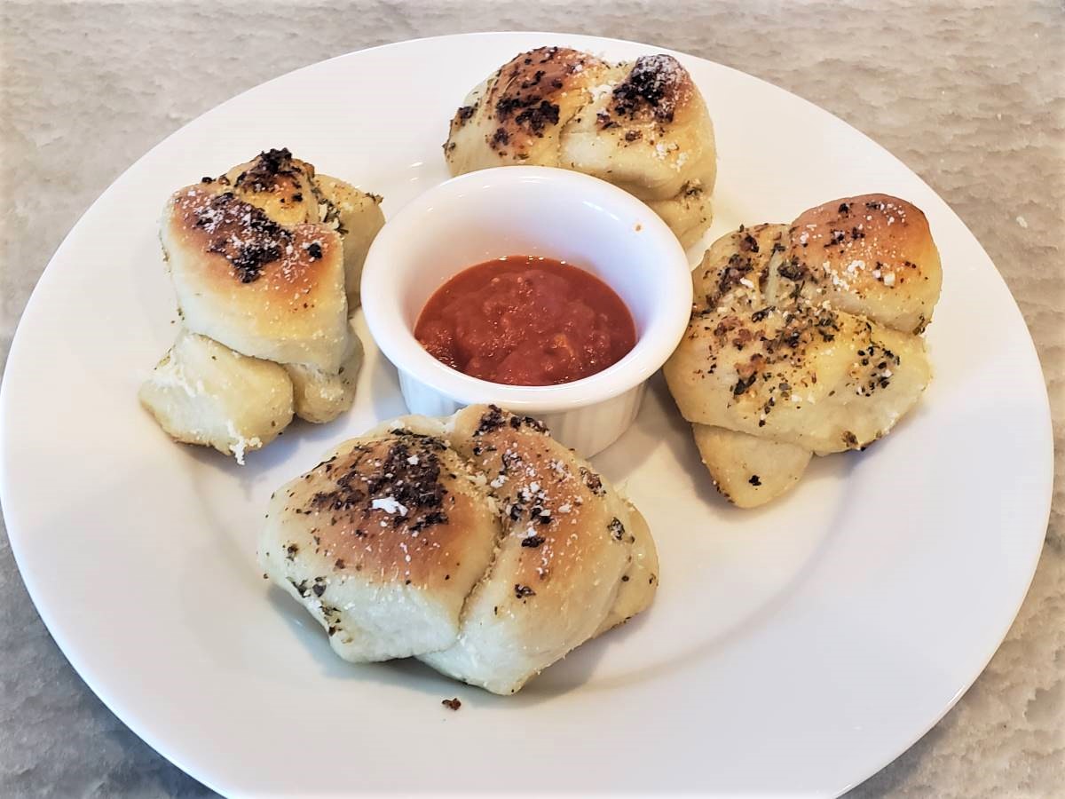 4 garlic knots on a plate with marinara dipping sauce