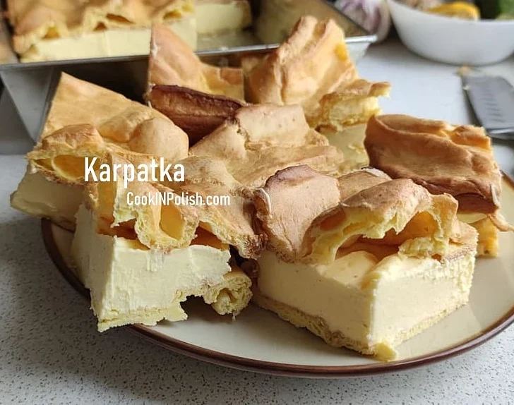 A plate of Karpatka, a traditional Polish cream pie made with choux pastry layers and a rich vanilla custard filling, served on a kitchen counter.