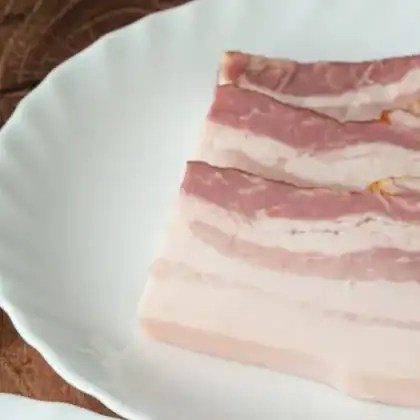 A slab of Polish boczek, smoked streaky pork belly with clear layers of fat and meat, on a white plate.