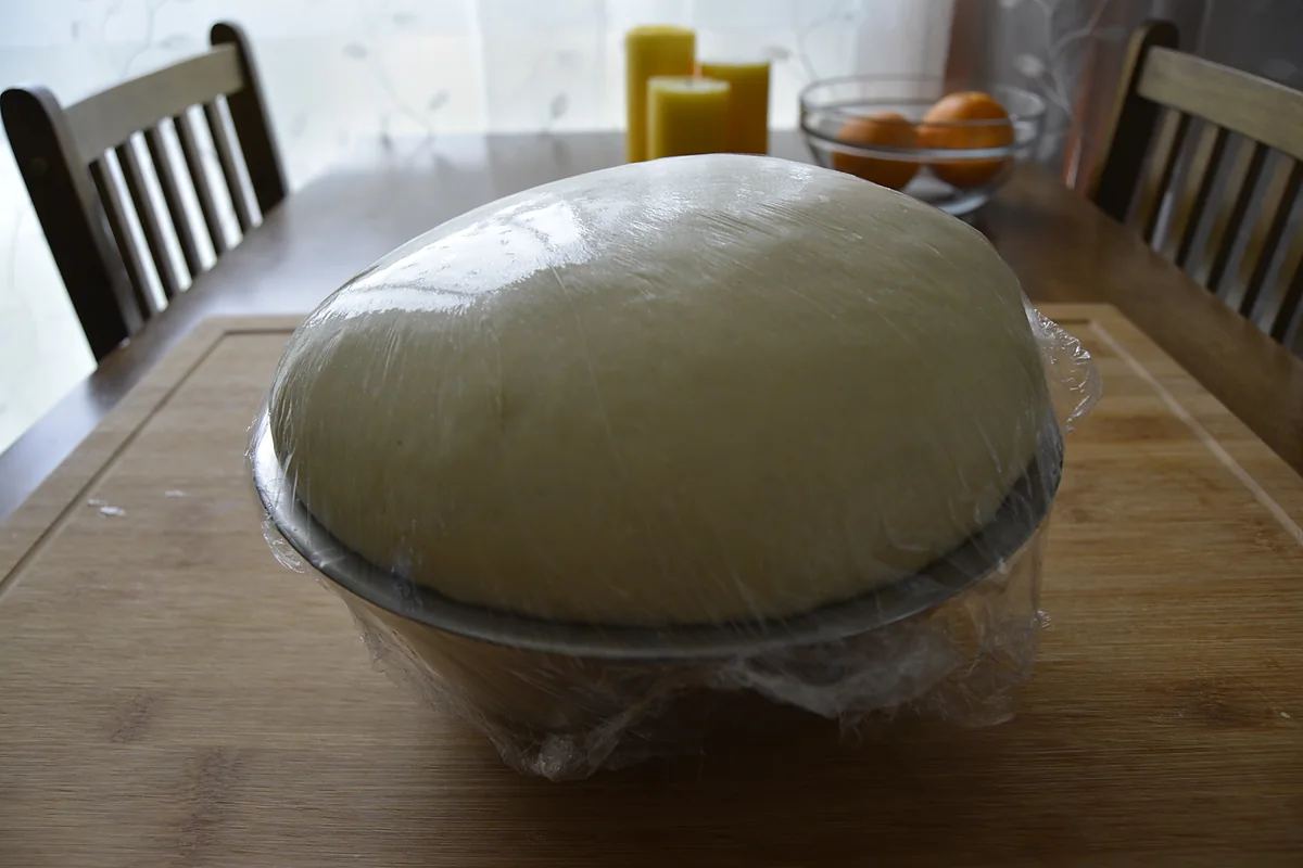 Chalka dough doubled in size under cling film in a bowl on a kitchen table