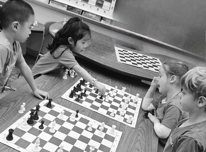Children playing chess at a classroom table during a Chess Rabbits after-school program in NYC, learning strategy and focus through hands-on lessons.
