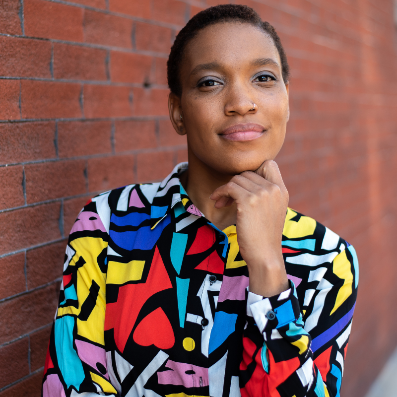 A dancemaker in a floral blouse with primary colors faces the camera with a confident smile.