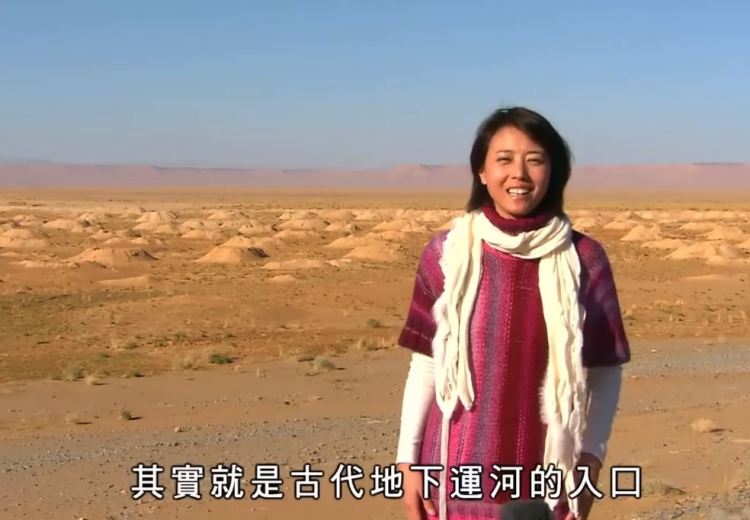 一名女性站在撒哈拉沙漠的背景前,面帶微笑,穿著色彩繽紛的衣物,周圍是一片廣闊的沙漠景觀,遠處可見沙丘的輪廓,畫面下方有中文文字。