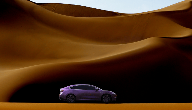 A purple LUXEED R7 car positioned against a backdrop of golden sand dunes, showcasing the vehicle's sleek design and color contrast with the desert landscape.
