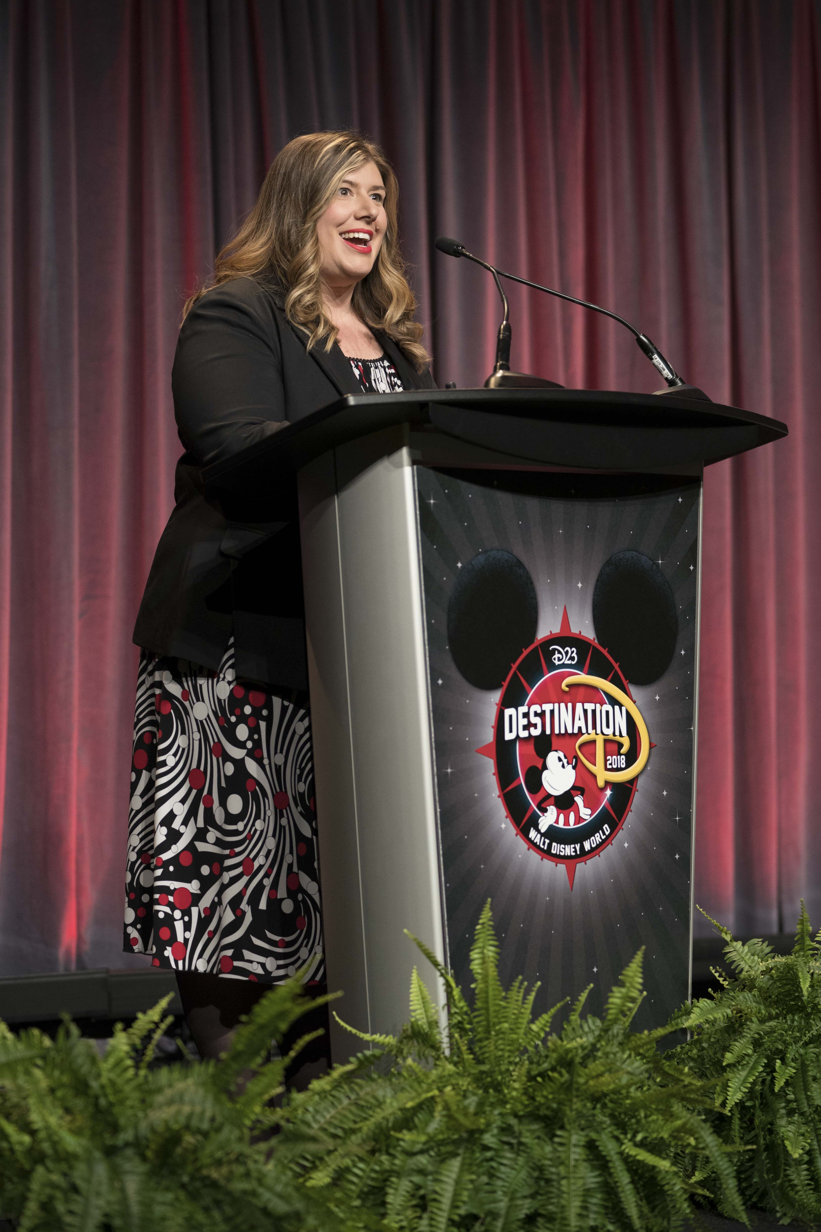 Kristin-Rodack-Stage.jpg: D23’s Kristin Rodack takes the stage to share exciting details about D23: The Official Disney Fan Club at D23’s Destination D: Celebrating Mickey Mouse, November 16-18, 2018 at Disney’s Contemporary Resort. © Disney
