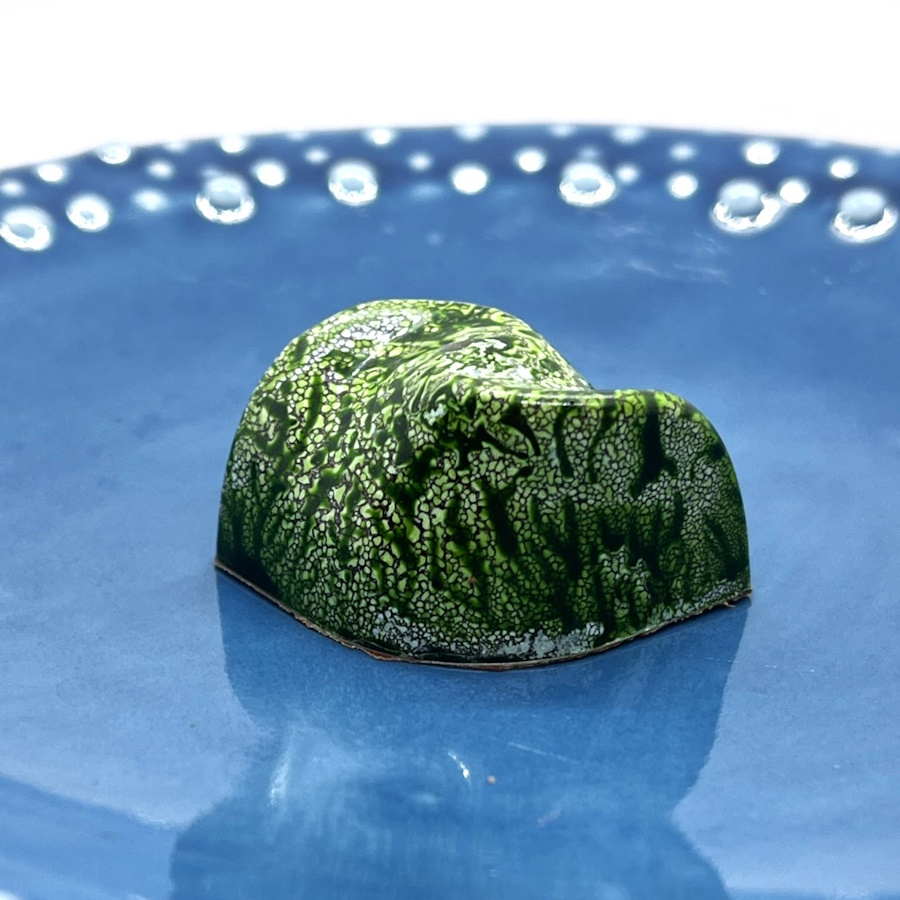 A green chocolate sits on a blue plate. The chocolate is in a squiggle design.