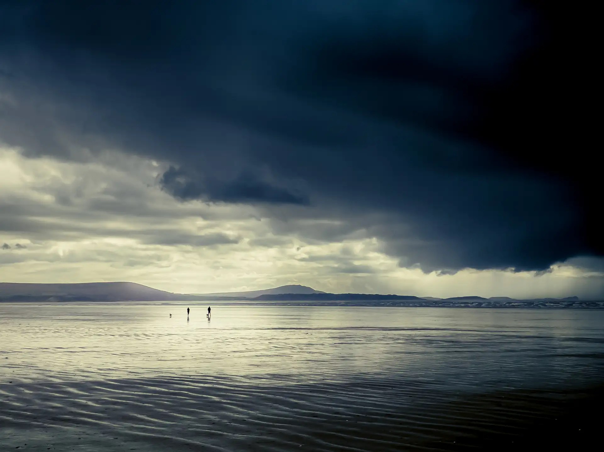Dog walkers on a large, sandy Welsh beach on a rainy day