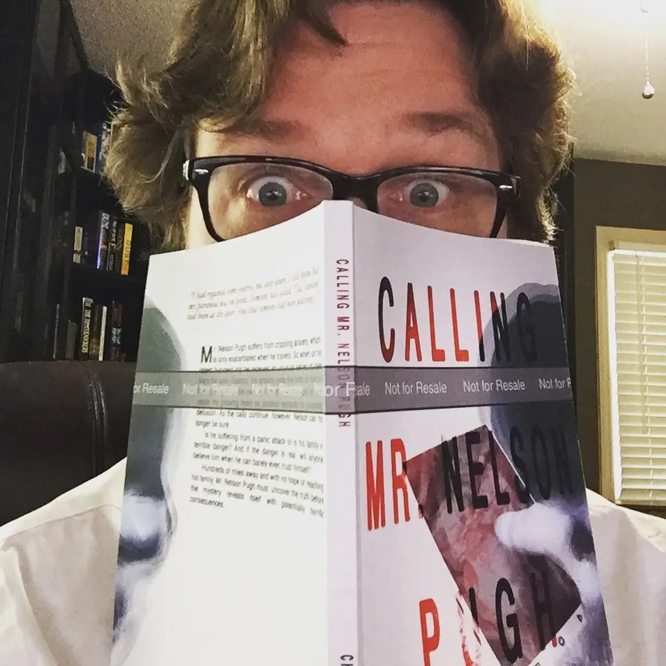 Image of Christopher Opyr with wavy brown hair, peeking over the top of a print proof of Calling Mr. Nelson Pugh.