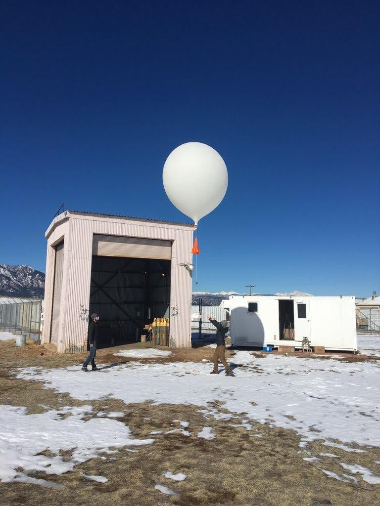 Two people releasing weather ballon with snowy mountains behind