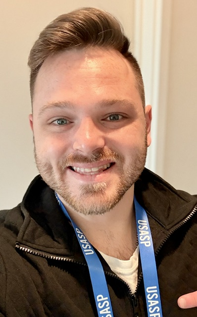Corben Parker, a head-and-shoulders portrait. He is smiling, in a dark jacket, wearing a blue USASP conference lanyard — the badge from the meeting this piece describes.