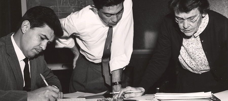 Three people pore over documents on a table.