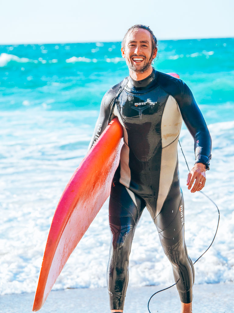 Surfer carrying a board on a Cornish beach with turquoise sea in the background