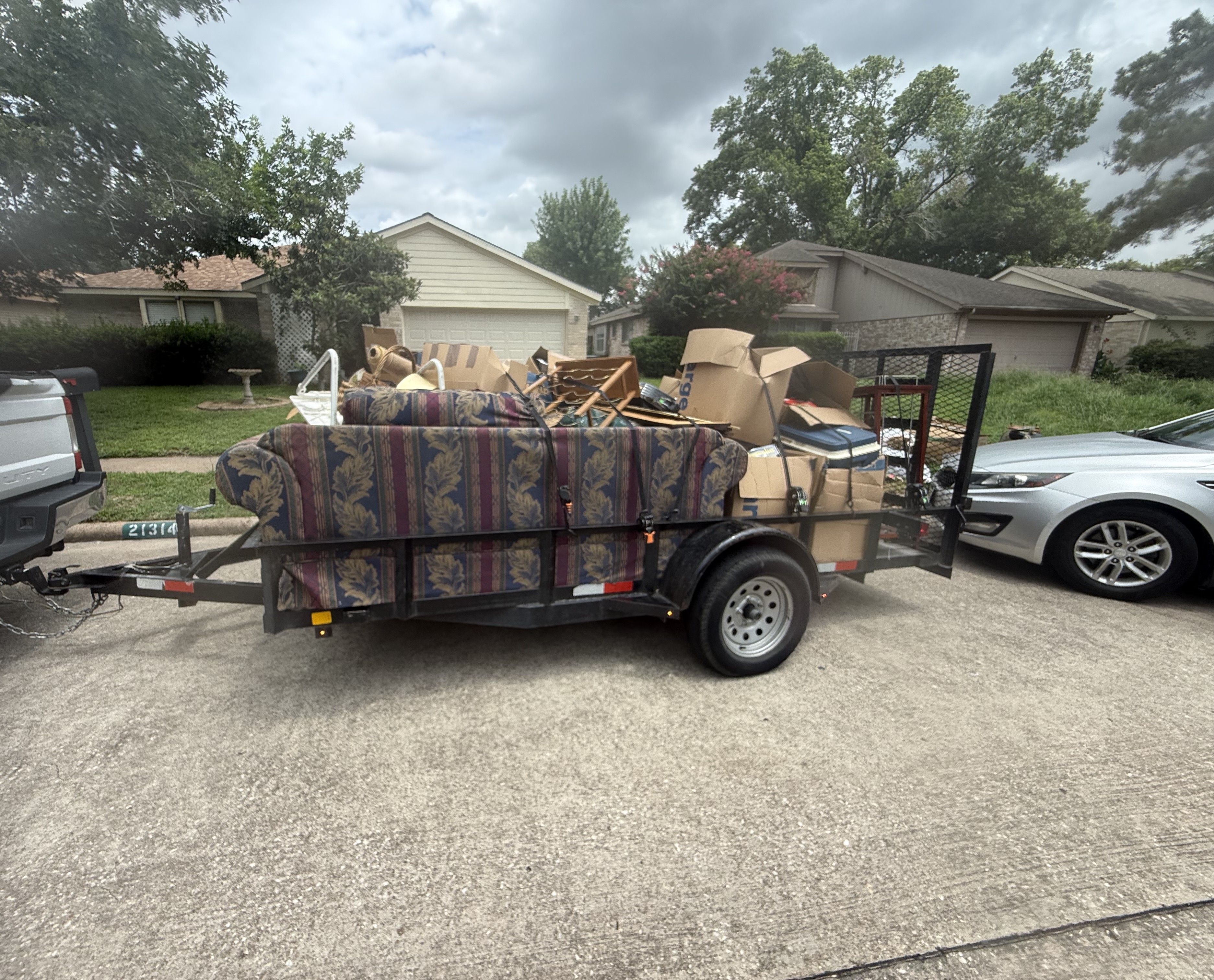Trailer loaded with an old floral couch, cardboard boxes and household junk outside a Houston area home