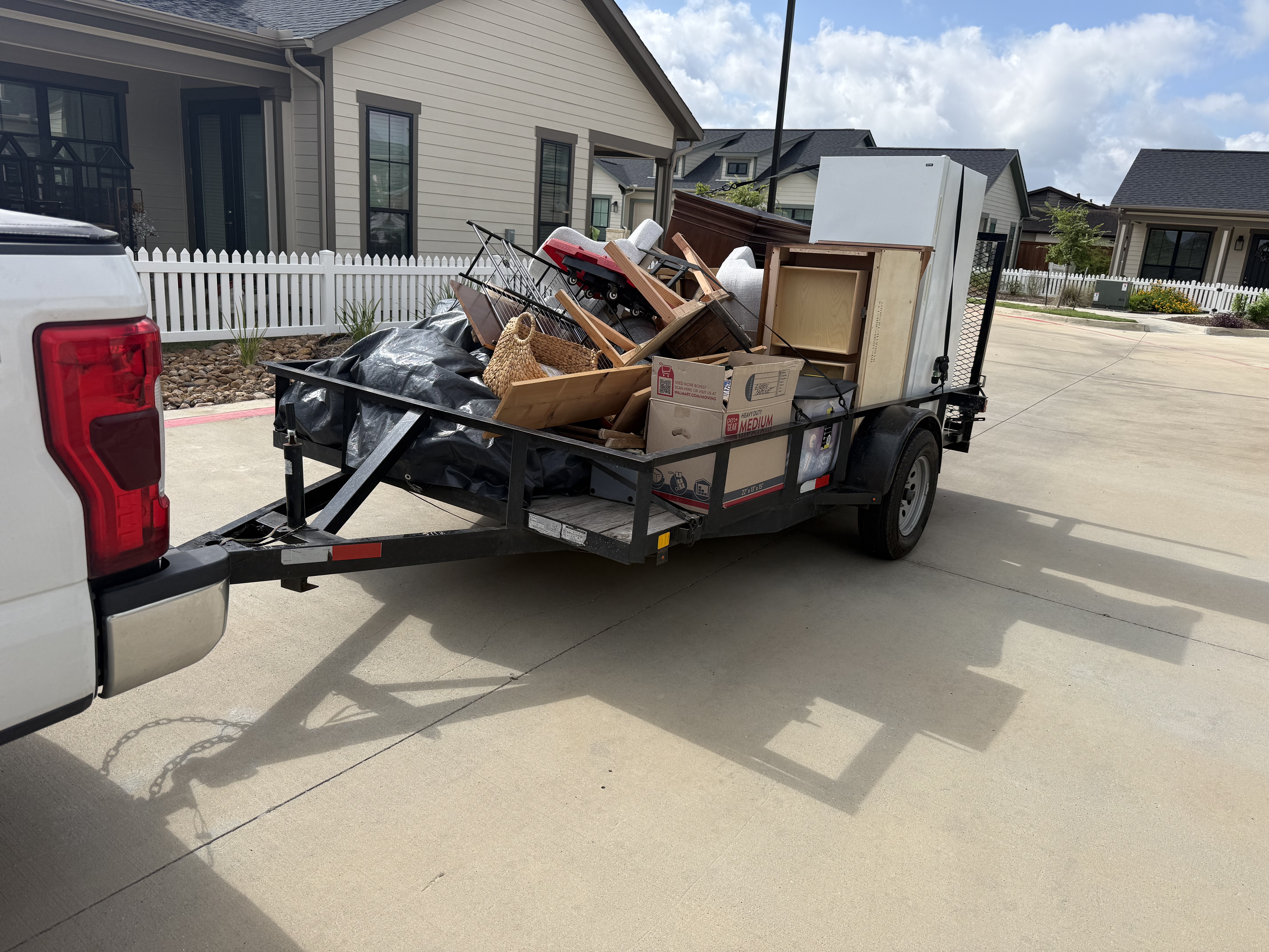 CJ's Junk Removal trailer fully loaded with furniture, a mini fridge, chairs and boxes outside a suburban home