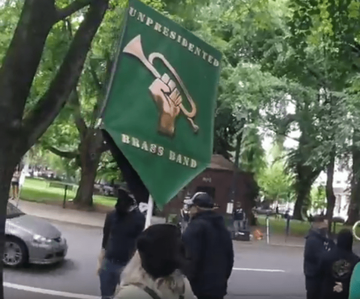 A large, slob of a man approaches a bystander, on the opposite side of Terry Schrunk, from where PP was, and confronts a man, in front of a Brass band.