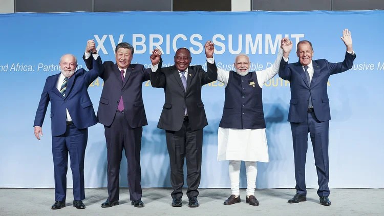 Leaders of BRICS countries at the XV BRICS Summit, raising their hands in celebration against a backdrop featuring the summit theme.