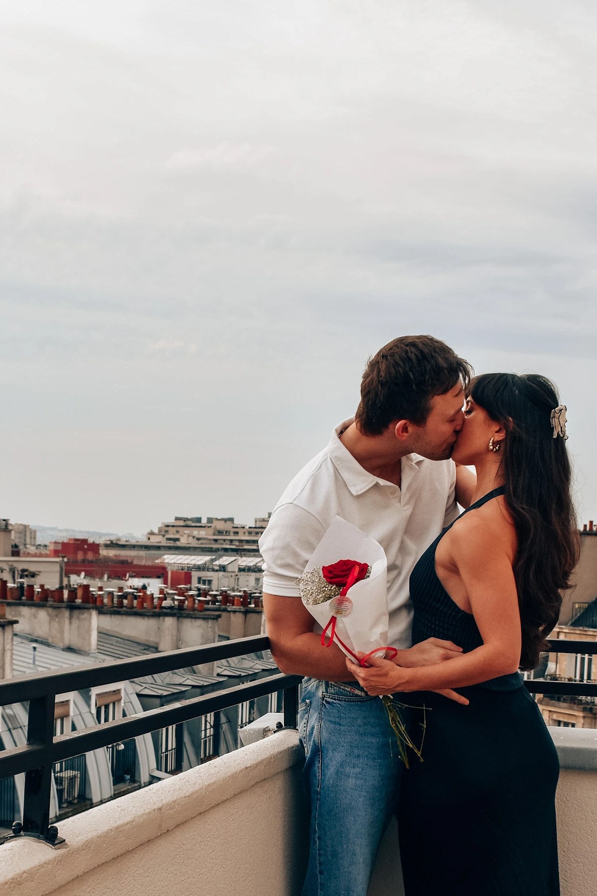 A couple exchanging a kiss on the balcony of a romantic paris hotel, holding a red rose