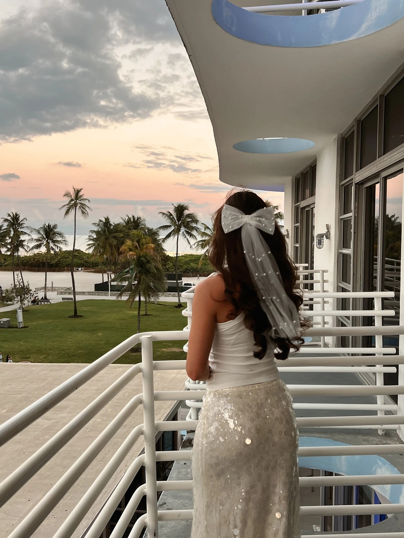 A girl in a bachelorette-style bow veil and all white outfit admiring the sunset in Miami