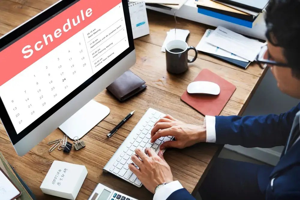 Employee scheduling software on a desktop monitor beside a wall calendar