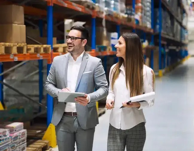 Vendor manager and contractor reviewing service paperwork in a warehouse aisle
