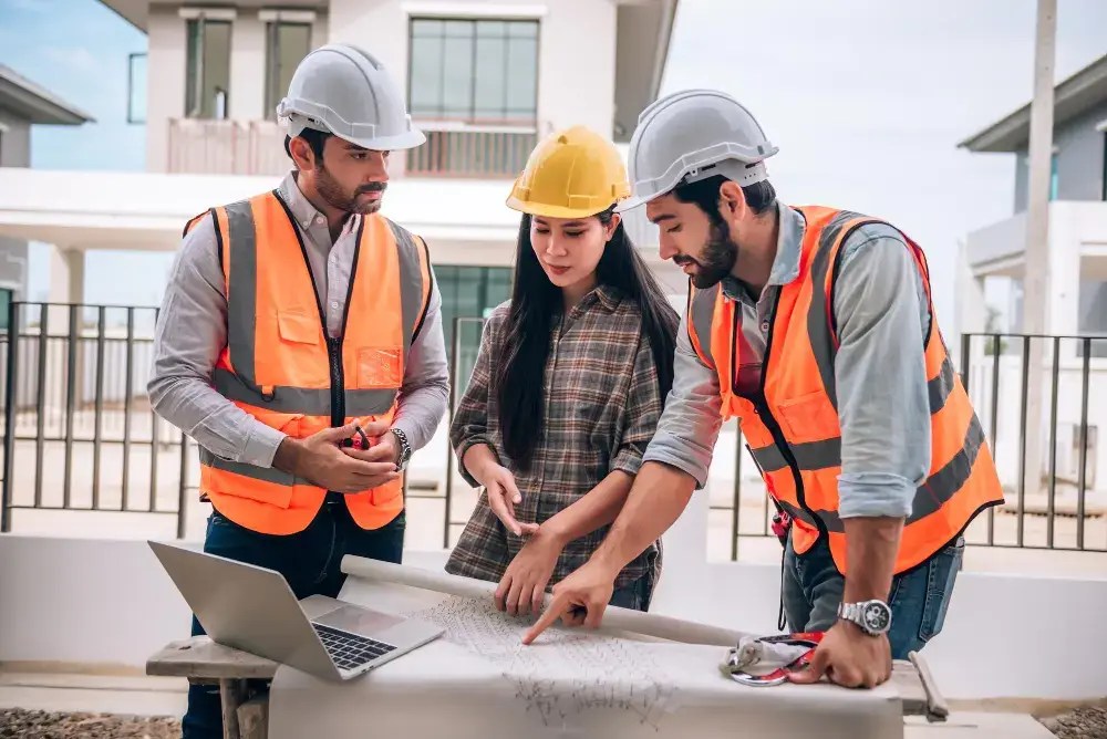 Site crew in hi-vis vests reviewing work orders on a laptop at a job site