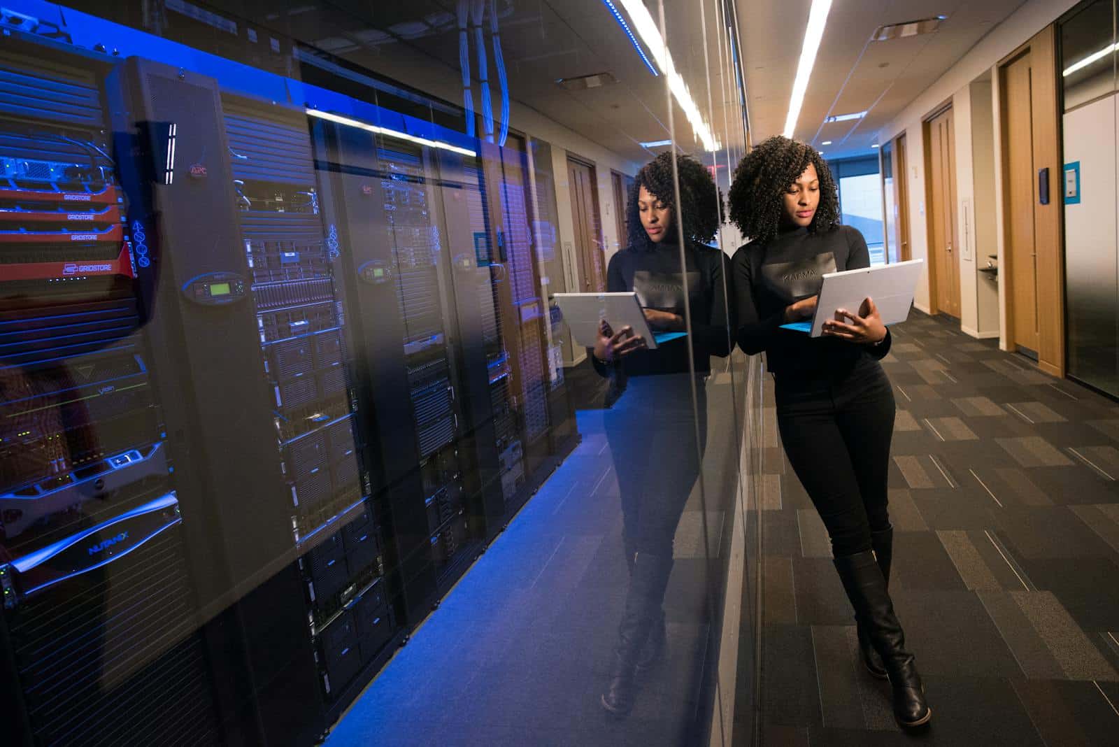 A woman using a laptop navigating a contemporary data center with mirrored servers showing the use of cloud build technologies.