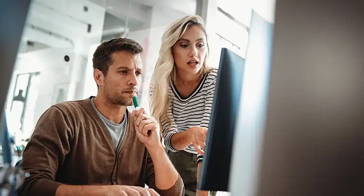 Two coworkers using a desktop computer discussing development