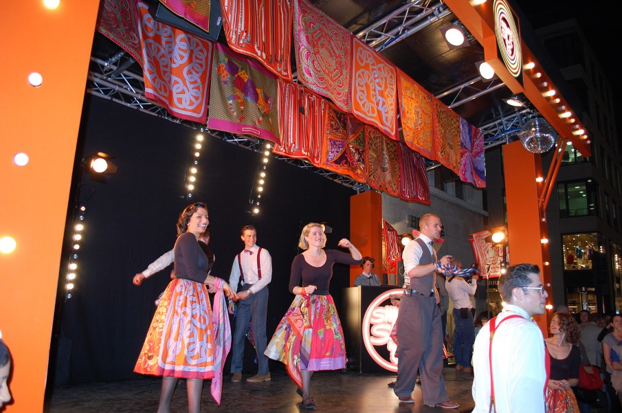 Bailarinas con faldas hechas de pañuelos de Hermès actuando en el escenario callejero de la marca